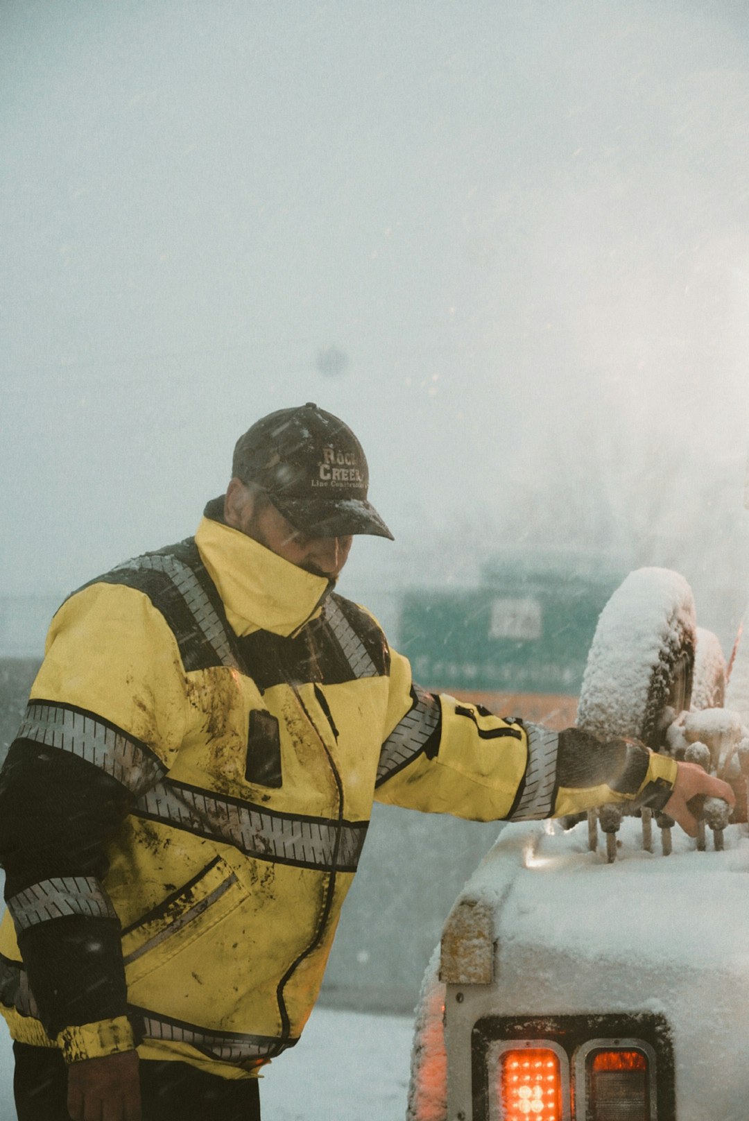 a-man-in-a-yellow-jacket-standing-next-to-a-car-covered-in-snow-q6r0zib78ww